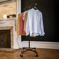 Monroe Trades mobile clothing rack displaying women's shirts and sweaters in front of a fireplace
